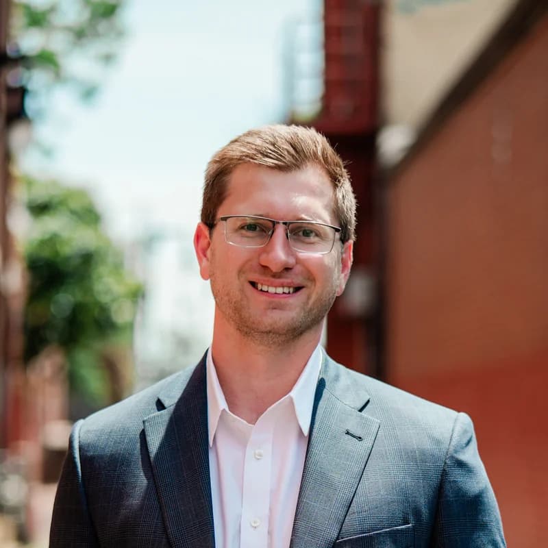Caleb Claussen, Wichita Realtor, smiling in a blazer in an Old Town alley